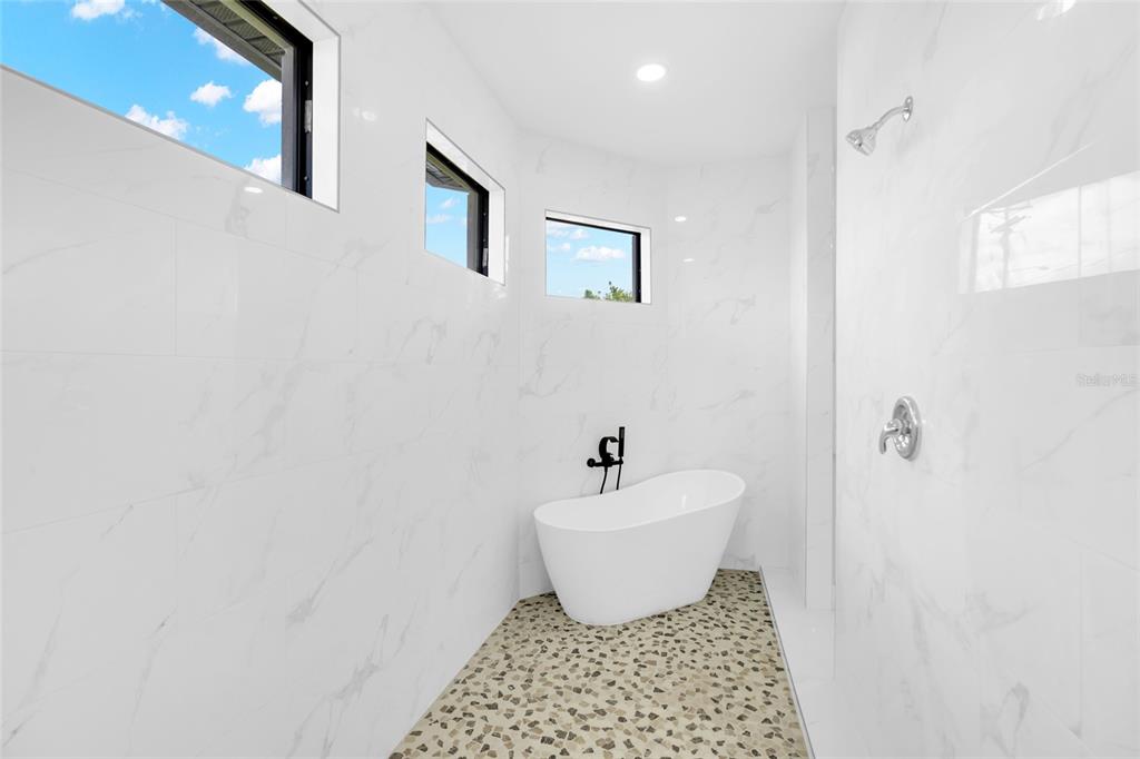 A modern bathroom features a freestanding tub, a walk-in shower, and white marble-look wall tiles — 2915 23RD STREET SW, LEHIGH ACRES, FL