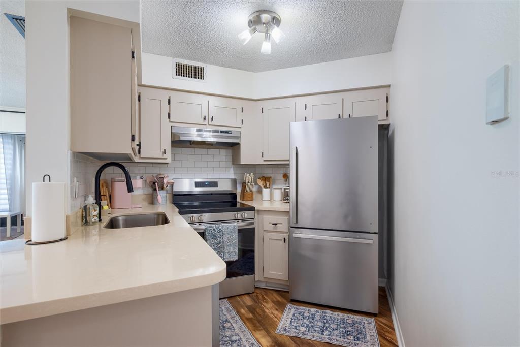 A kitchen features light-colored cabinets, stainless steel appliances, a subway tile backsplash, and wood flooring — 3806 SOUTHPOINTE DRIVE UNIT L4, ORLANDO, FL