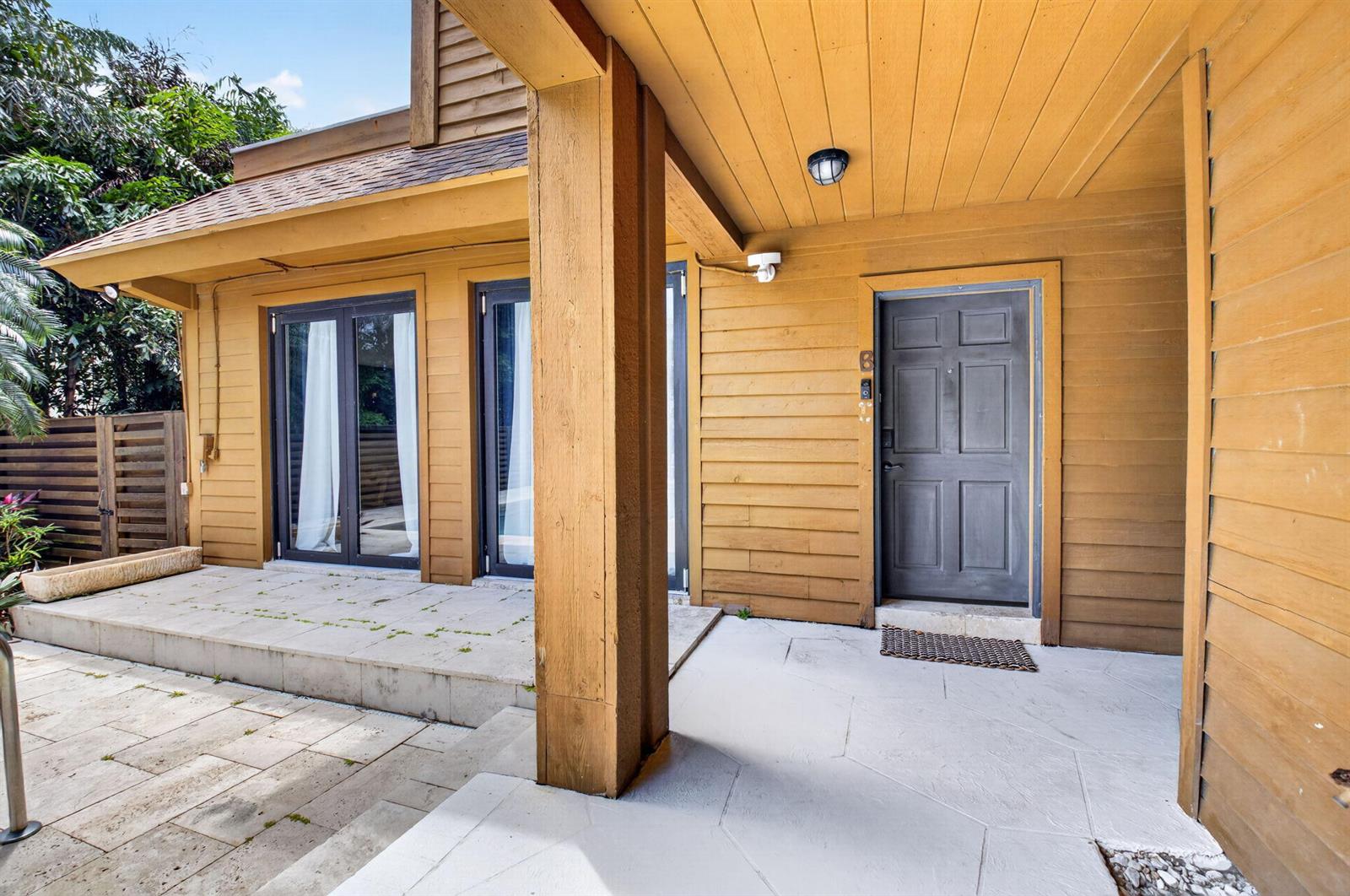 A covered patio with light stone flooring leads to a dark door and glass doors — 122 Andrews Avenue # B, Delray Beach FL 33483, DELRAY BEACH, FL