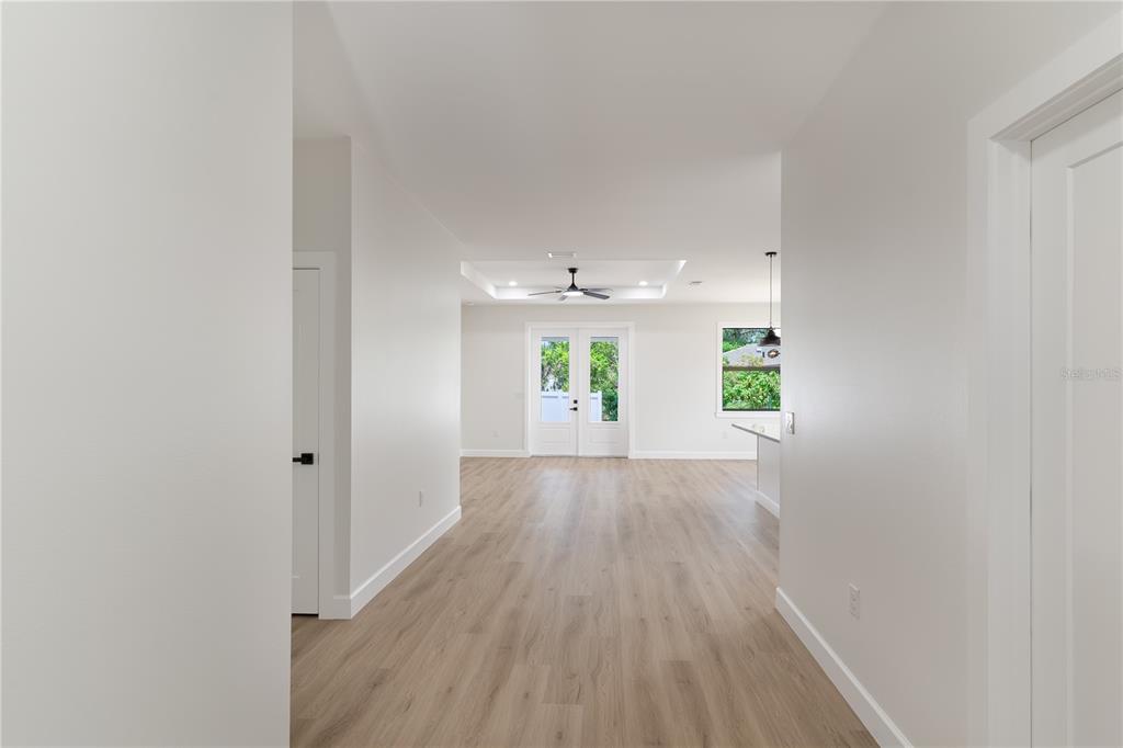 A hallway with light wood-look flooring leads to an open living area with French doors — 923 CUMBERLAND ROAD, VENICE, FL