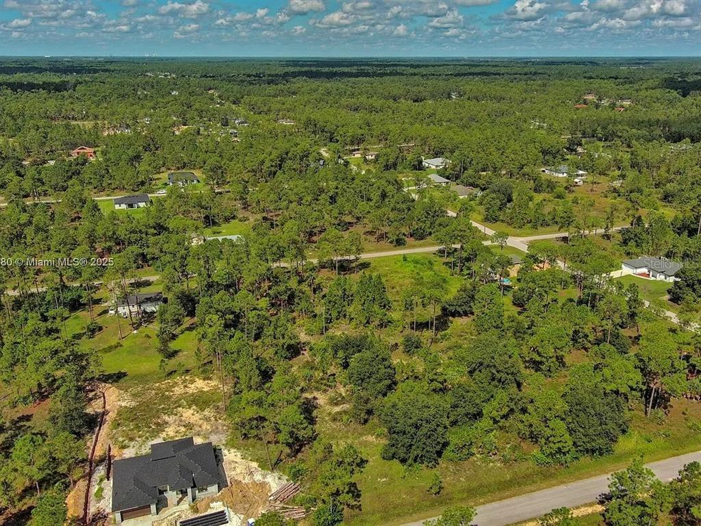 An aerial view shows a house under construction surrounded by a wooded residential area — 1219 WASHINGTON AVENUE, LEHIGH ACRES, FL