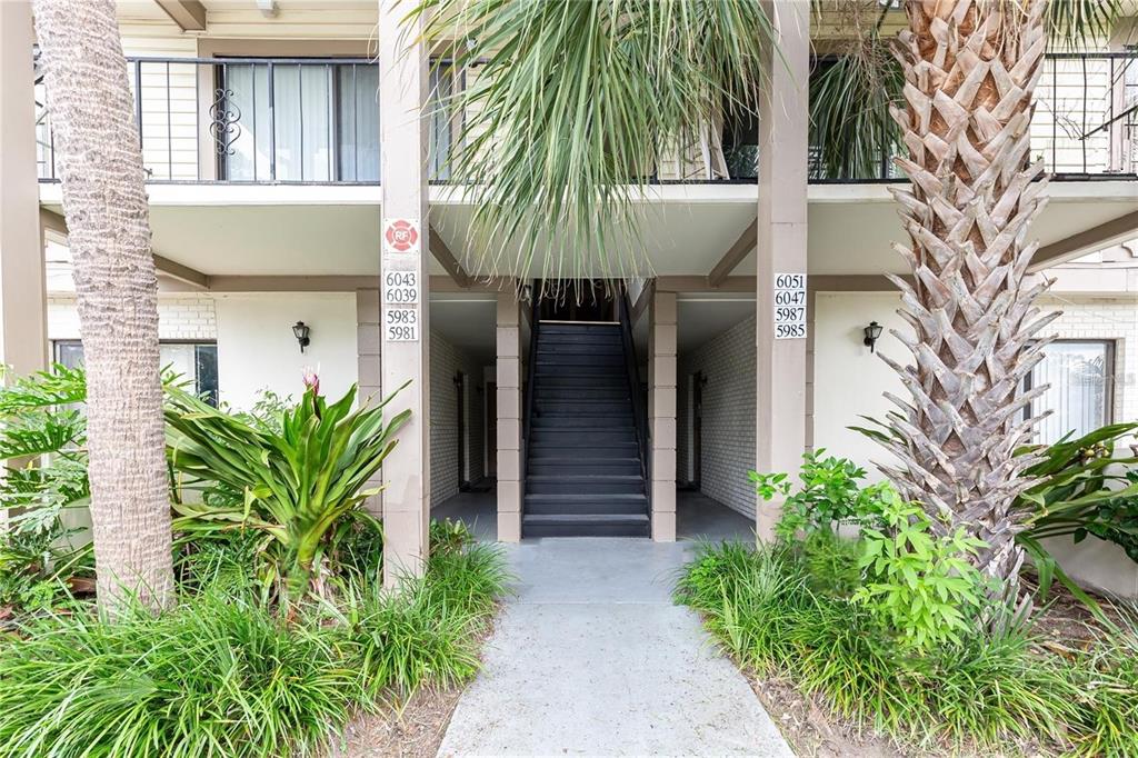 A concrete walkway leads to a central staircase between two apartment building columns with signage — 6039 VILLAGE CIRCLE BLDG C, ORLANDO, FL