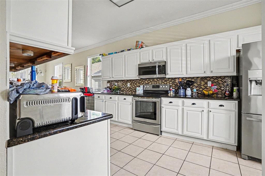 A kitchen features white cabinets, stainless steel appliances, a tiled backsplash, and light floor tiles — 615 COPELAND DRIVE, HAINES CITY, FL