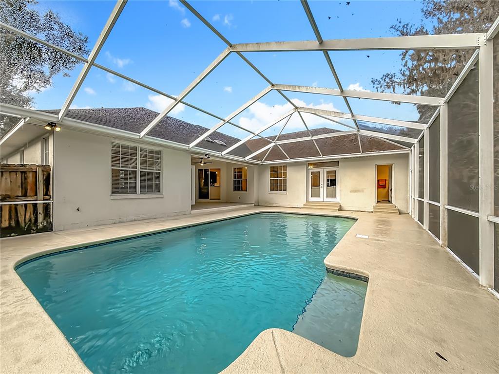 A screened-in swimming pool sits on a concrete patio behind a single-story house — 2614 SE 25TH COURT, OCALA, FL