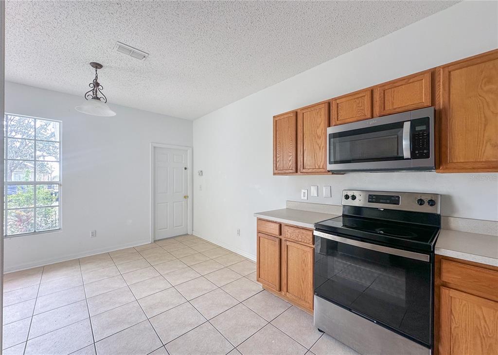 A kitchen with wood cabinets, stainless steel appliances, tile flooring, and an adjacent dining area — 402 SUNSET VIEW DRIVE, DAVENPORT, FL