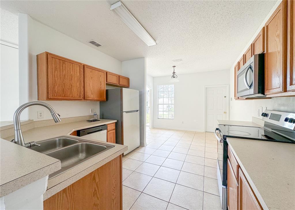 A kitchen with wood cabinets, light countertops, tile flooring, and a stainless steel refrigerator — 402 SUNSET VIEW DRIVE, DAVENPORT, FL