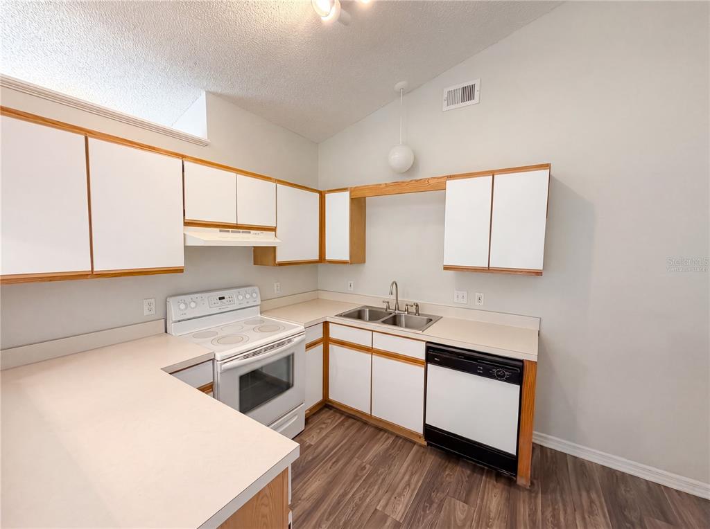 A kitchen features white cabinets with wood trim, laminate countertops, and white appliances — 114 PAMALA COURT, SANFORD, FL