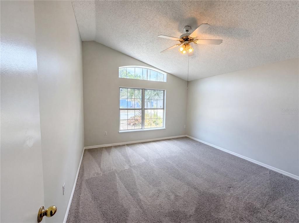 An empty bedroom features gray carpet, light-colored walls, a vaulted ceiling, and a ceiling fan — 114 PAMALA COURT, SANFORD, FL