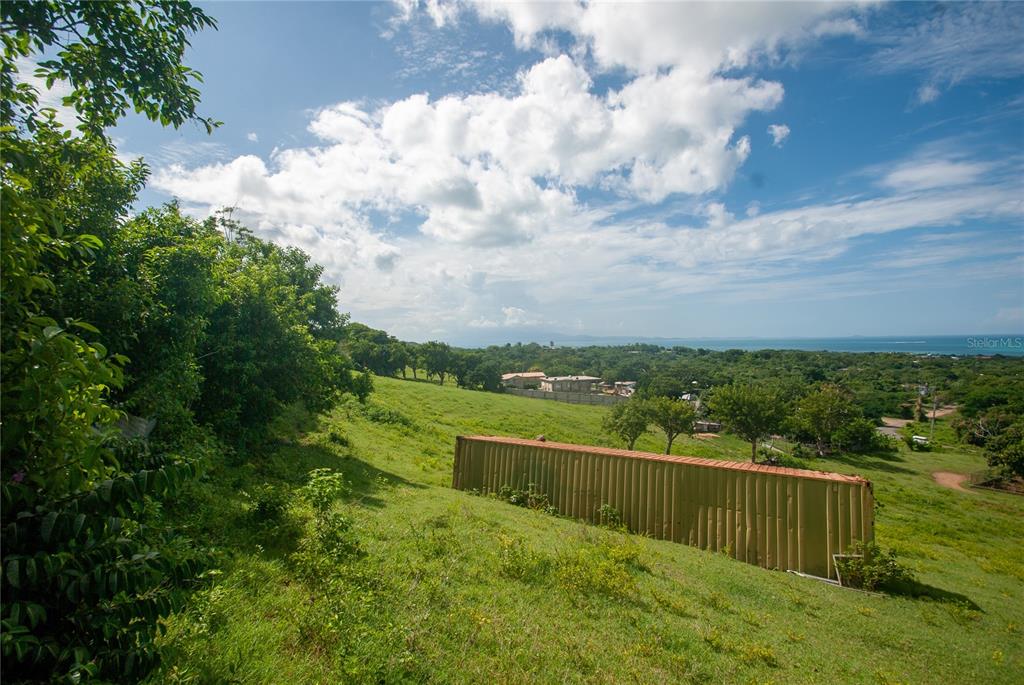 A grassy, sloping hillside features a large metal shipping container overlooking a distant coastal view — 14 CALLE 16, VIEQUES, PR