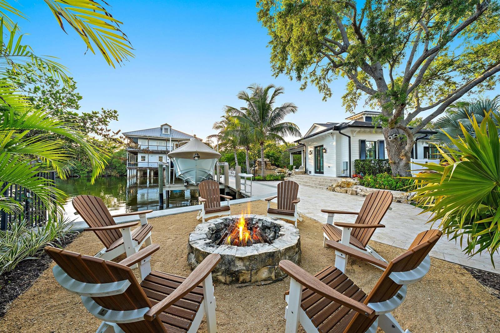 A stone fire pit surrounded by Adirondack chairs overlooks a waterfront dock with a boat — 942 Pompano Drive, Jupiter FL 33458, JUPITER, FL