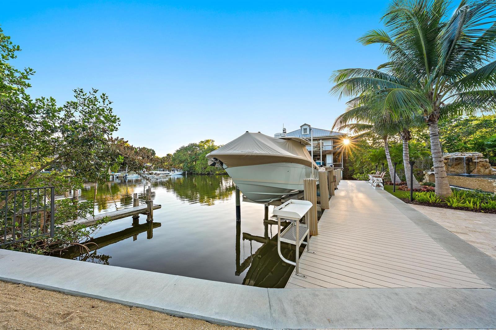 A boat on a lift sits at a dock next to a house and palm trees — 942 Pompano Drive, Jupiter FL 33458, JUPITER, FL