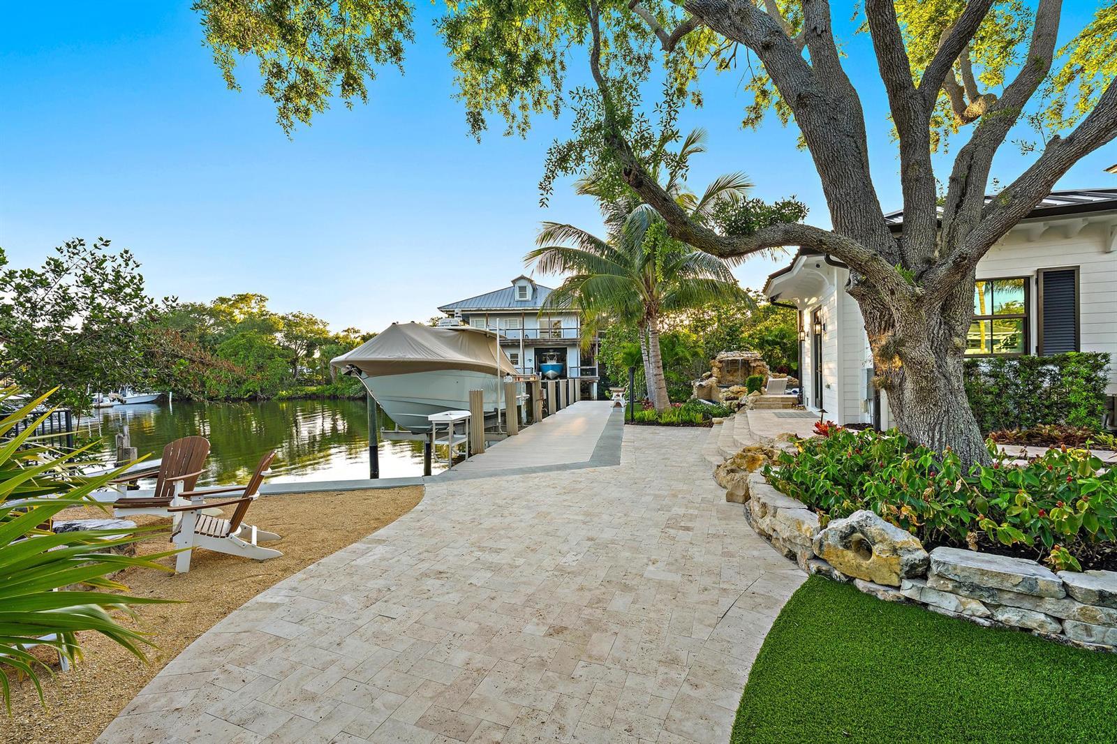 A paved walkway leads past a large tree toward a boat docked on a canal — 942 Pompano Drive, Jupiter FL 33458, JUPITER, FL