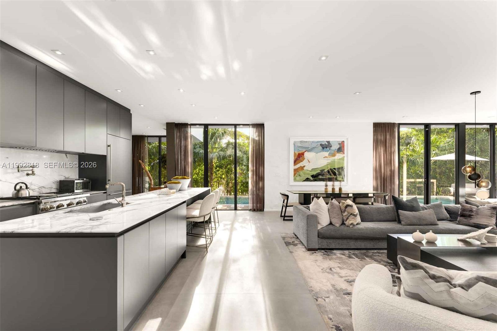 A modern open-concept kitchen and living area features a marble island and floor-to-ceiling windows — 121 2nd Dilido Ter. Share A, Miami Beach FL 33139, MIAMI BEACH, FL