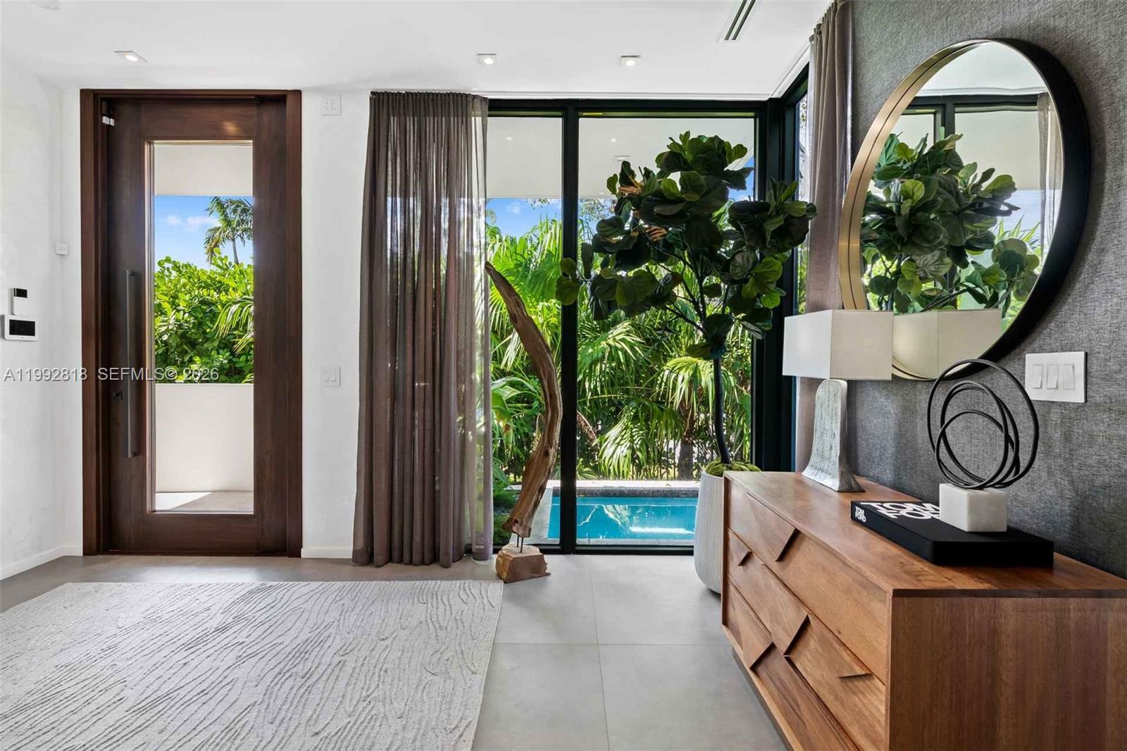 A modern entryway features a wooden door, a console table, a mirror, and a pool view — 121 2nd Dilido Ter. Share A, Miami Beach FL 33139, MIAMI BEACH, FL
