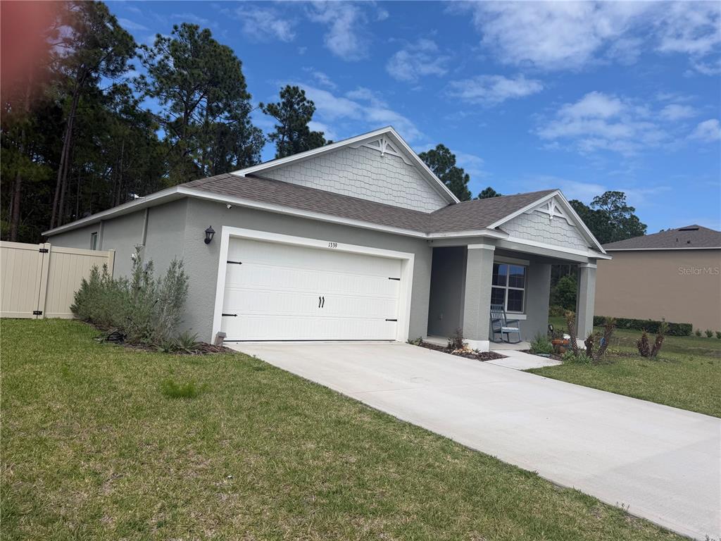 A one-story suburban house with a gray stucco exterior, white garage door, and shingled roof — 1339 MORNING WALK DRIVE, ORMOND BEACH, FL