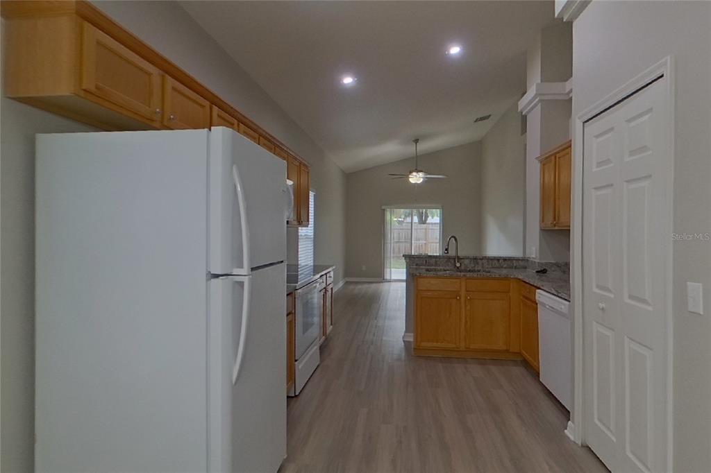 A kitchen features light wood cabinets, granite countertops, white appliances, and light-colored wood-look flooring — 2143 KAYLAS COURT, ORLANDO, FL