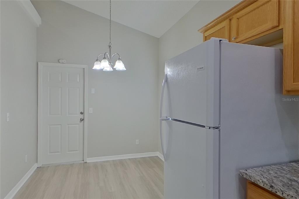 A kitchen dining area features light wood-look flooring, a white refrigerator, and a hanging chandelier — 2143 KAYLAS COURT, ORLANDO, FL