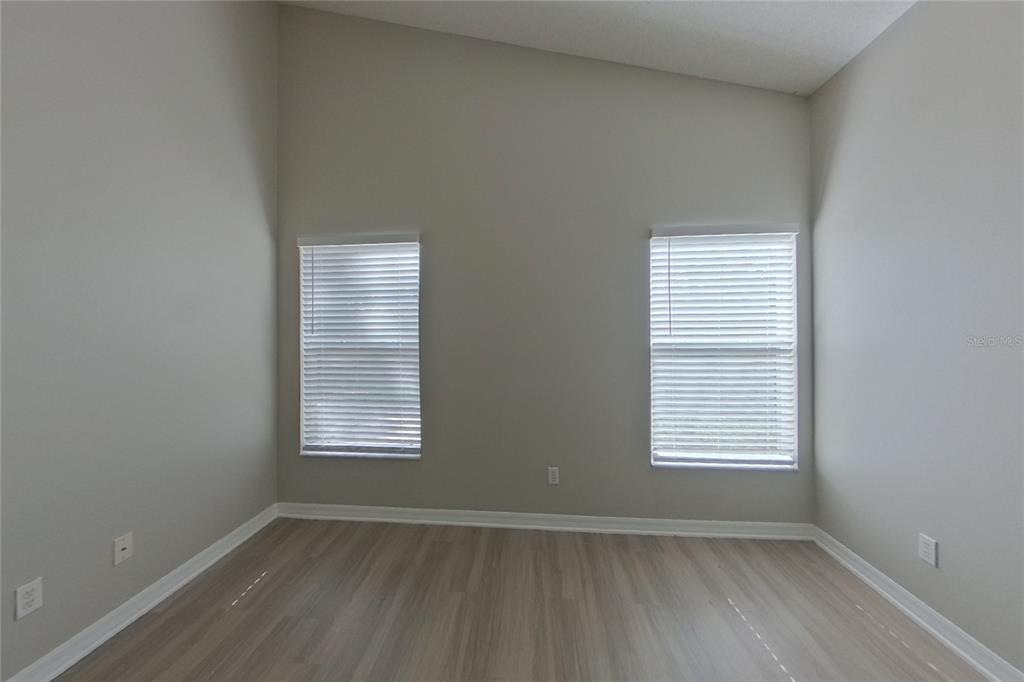 An empty room features light gray walls, wood-look flooring, and two windows with white blinds — 2143 KAYLAS COURT, ORLANDO, FL