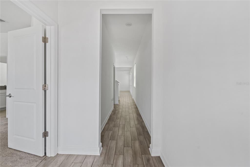 A hallway with light-colored walls and wood-look tile flooring leads toward a distant window — 2999 ADDISON BOULEVARD, ST CLOUD, FL