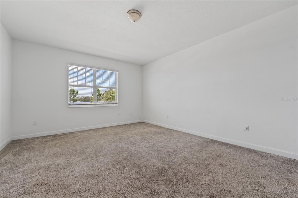 An empty bedroom features white walls, beige carpeting, a ceiling light, and a window view — 2999 ADDISON BOULEVARD, ST CLOUD, FL