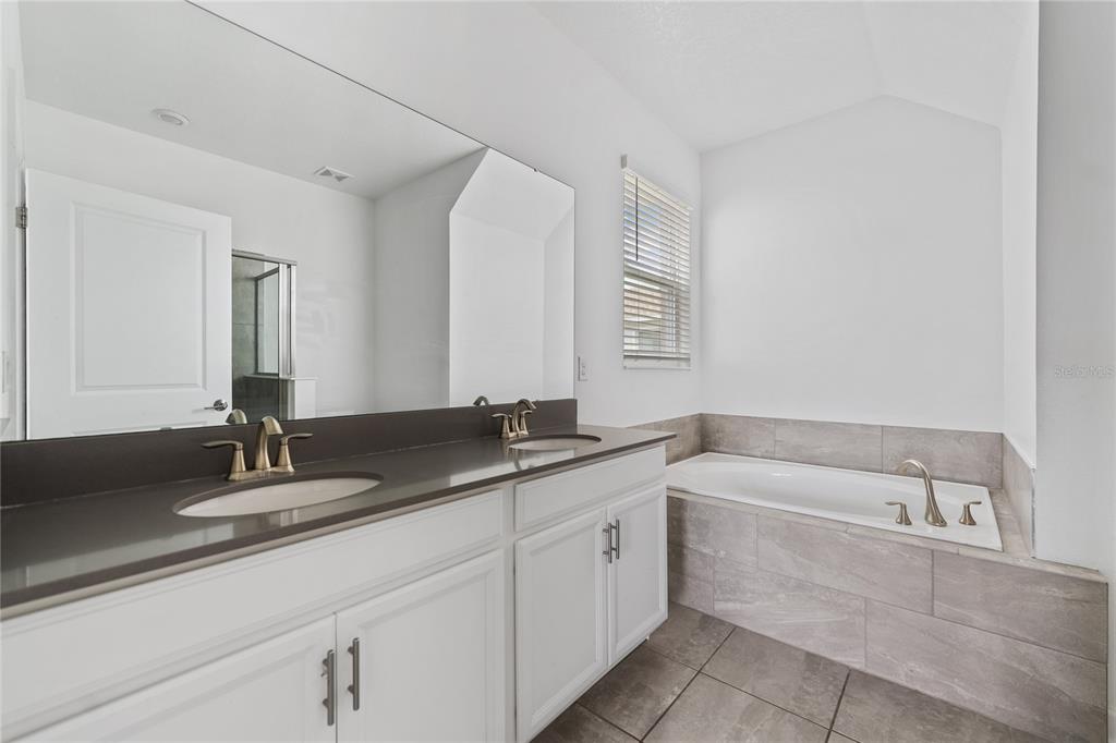 A bathroom features a double vanity with a dark countertop and a tiled soaking tub — 2999 ADDISON BOULEVARD, ST CLOUD, FL