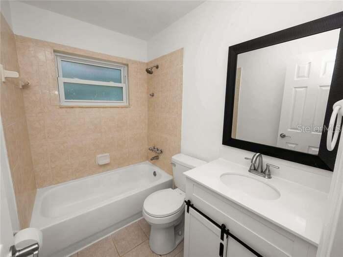 A bathroom features a white vanity, a toilet, and a bathtub with beige tiled walls — 5134 W HARVARD STREET W, LAKELAND, FL