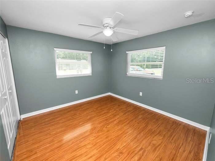 An empty bedroom features blue-gray walls, wood-look flooring, two windows, and a ceiling fan — 5134 W HARVARD STREET W, LAKELAND, FL