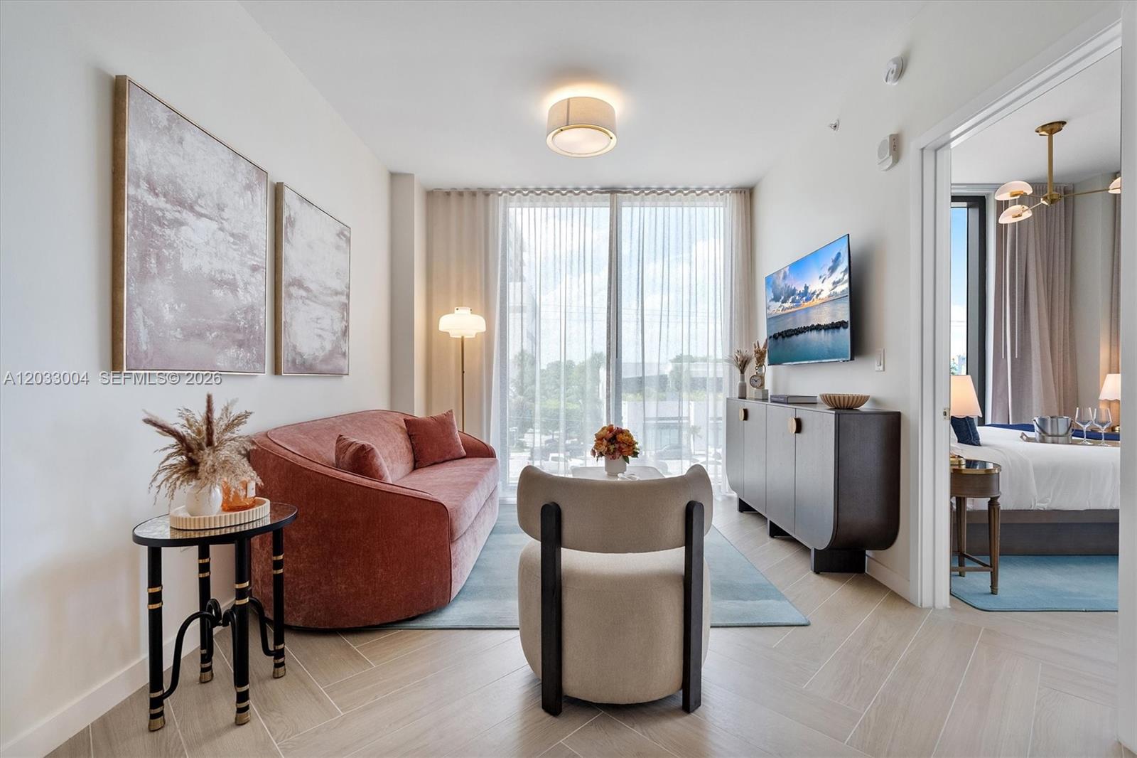 A living room features a curved pink sofa, a beige accent chair, and a television — 2700 NW 2nd Ave # 230, Miami FL 33127, MIAMI, FL