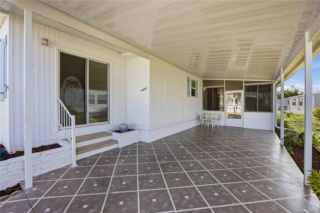 A covered patio with a patterned concrete floor and steps leading to a sliding glass door — 16 N GRANADA PLAZA, ENGLEWOOD, FL