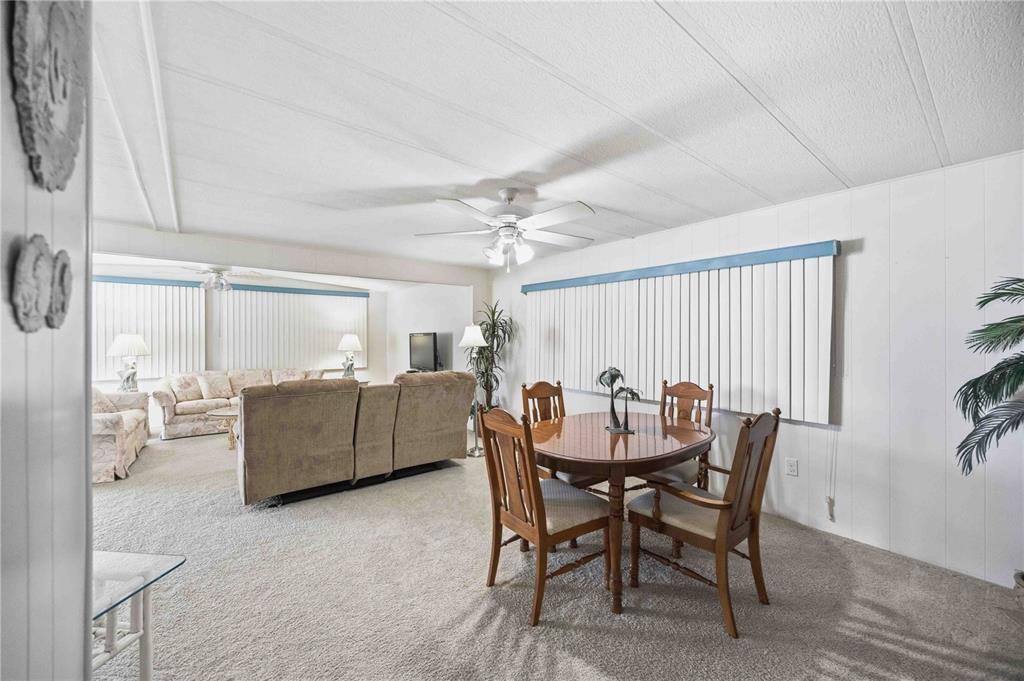 A living and dining area with carpeted floors, a ceiling fan, and vertical window blinds — 16 N GRANADA PLAZA, ENGLEWOOD, FL