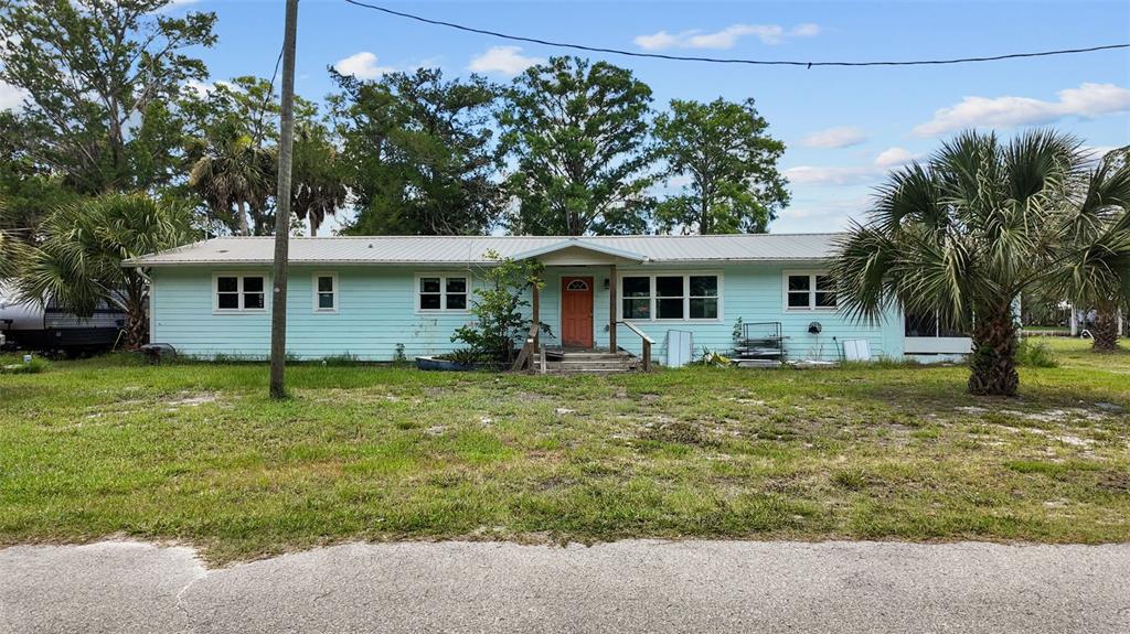 A single-story light blue house with a metal roof and an orange front door — 306 SE 256 STREET, SUWANNEE, FL