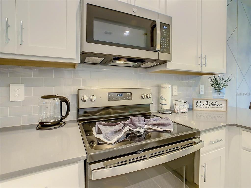 A kitchen features white cabinets, a stainless steel microwave, a glass-top stove, and gray countertops — 8853 CABOT CLIFFS DRIVE UNIT 104, DAVENPORT, FL