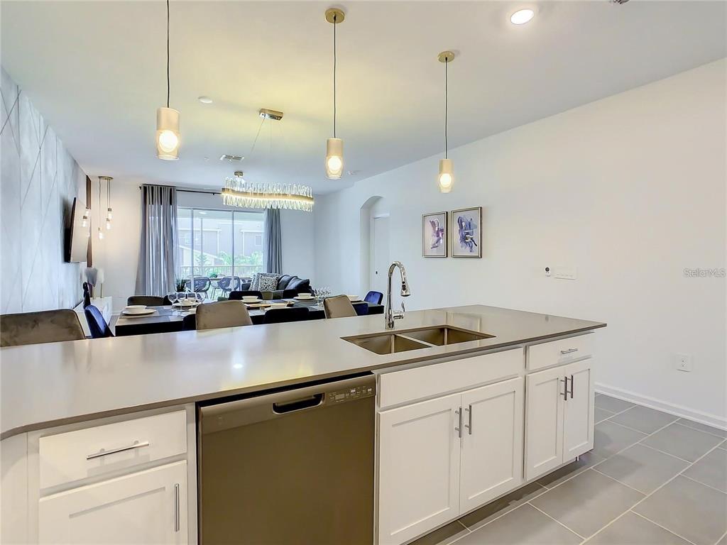 A modern kitchen with white cabinets and a stainless steel dishwasher overlooks a dining area — 8853 CABOT CLIFFS DRIVE UNIT 104, DAVENPORT, FL