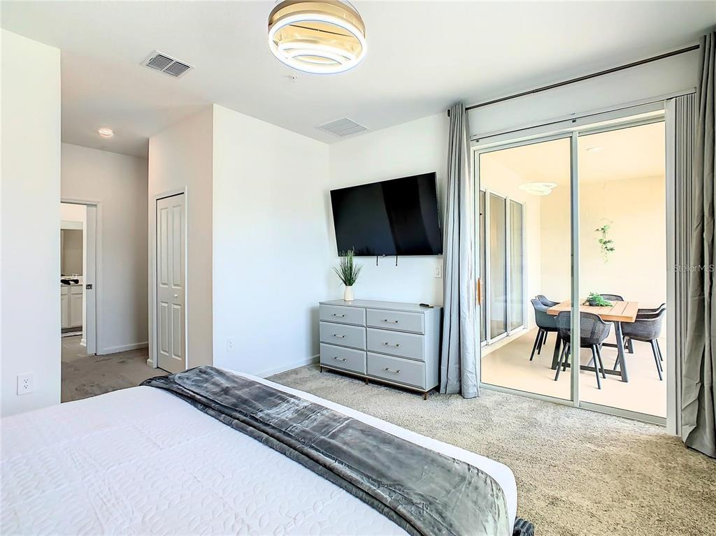 A bedroom features a bed, a gray dresser with a television, and sliding glass doors — 8853 CABOT CLIFFS DRIVE UNIT 104, DAVENPORT, FL