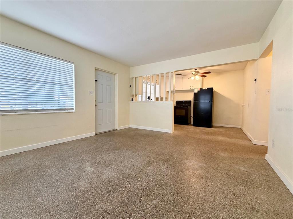 A living room with terrazzo flooring leads to an open kitchen with a black refrigerator — 513 AVENUE J SE, WINTER HAVEN, FL