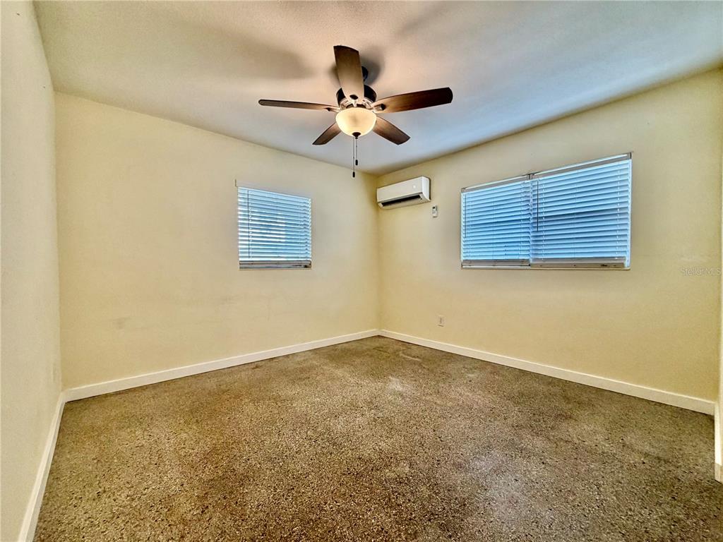 An empty bedroom features beige walls, carpeted flooring, a ceiling fan, and a wall-mounted AC unit — 513 AVENUE J SE, WINTER HAVEN, FL
