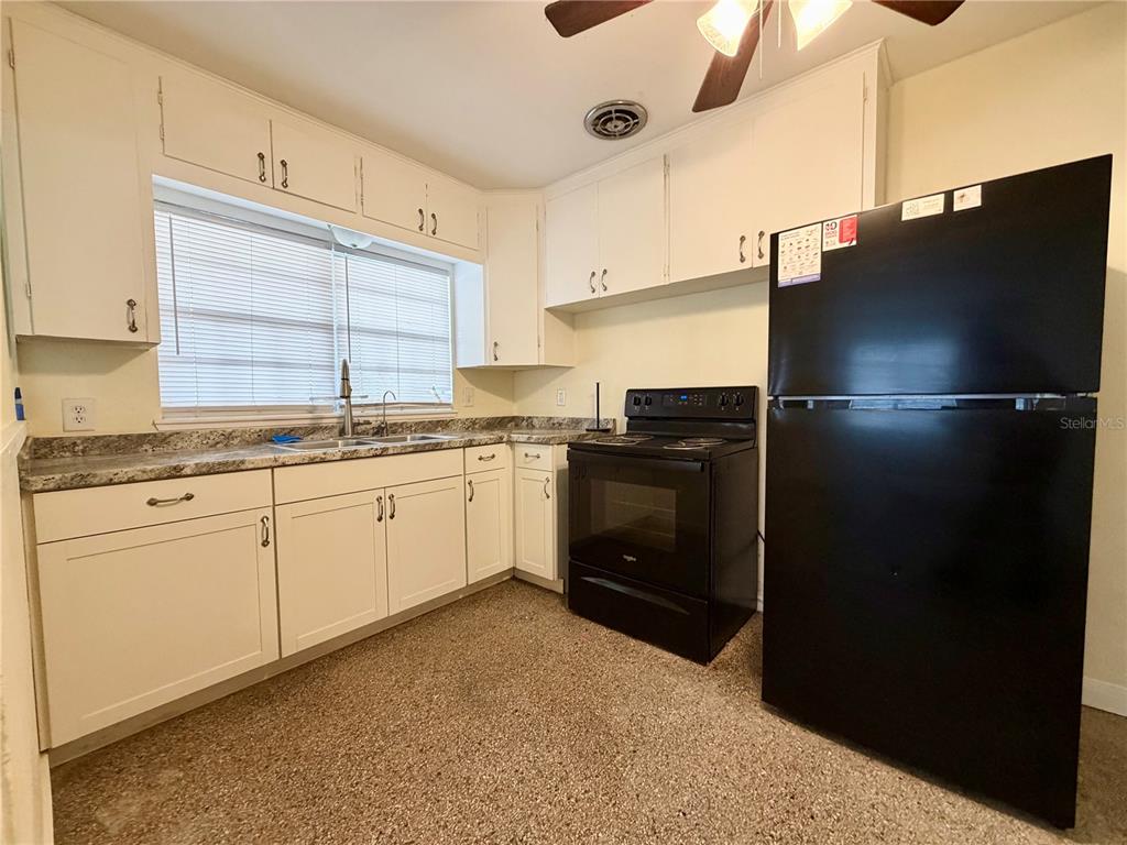 A kitchen features white cabinets, a black refrigerator, a black stove, and speckled countertops — 513 AVENUE J SE, WINTER HAVEN, FL