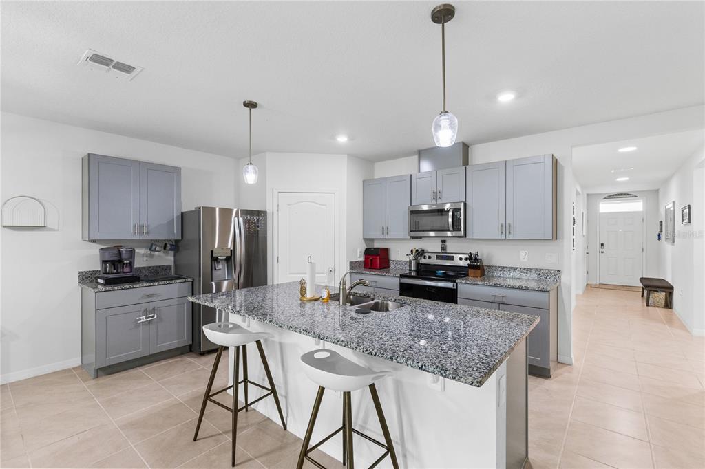 A kitchen features gray cabinets, granite countertops, a central island with stools, and stainless appliances — 452 BARONESS WAY, DELAND, FL