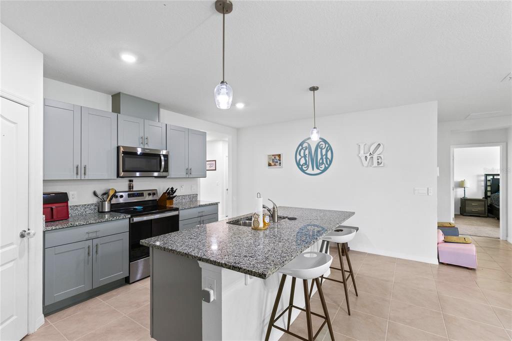 A kitchen features gray cabinets, granite countertops, a central island, and two white bar stools — 452 BARONESS WAY, DELAND, FL