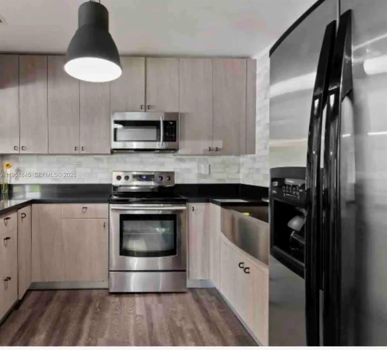 A kitchen features light wood cabinets, stainless steel appliances, a black countertop, and wood flooring — 3008 NW 13th St, Miami FL 33125, MIAMI, FL