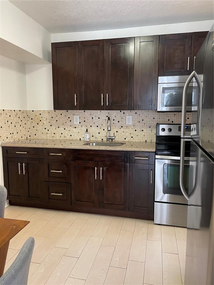 A kitchen features dark wood cabinets, stainless steel appliances, and a mosaic tile backsplash — 221 SW 9 AVE # 2, Miami FL 33130, MIAMI, FL