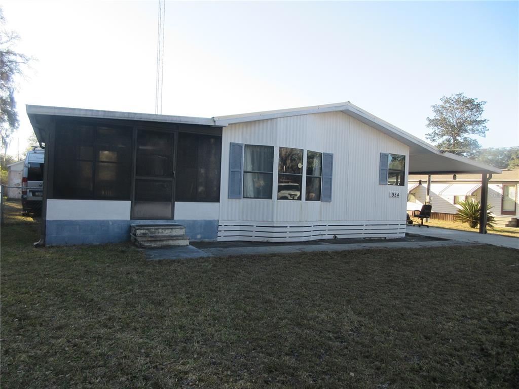 A single-story manufactured home with a screened-in porch, white siding, and an attached carport — 1984 SE 171ST COURT, SILVER SPRINGS, FL