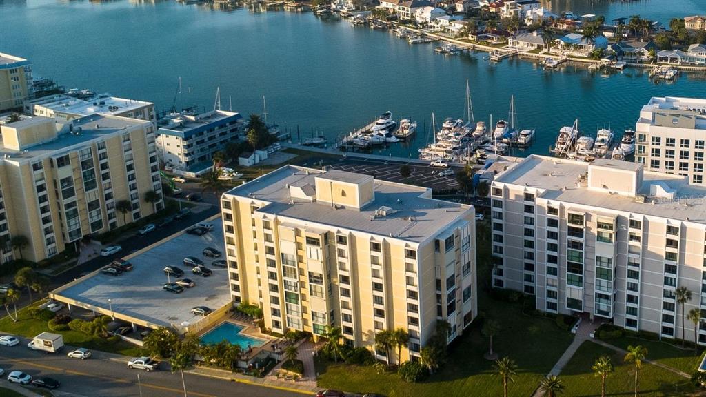 An aerial view shows multi-story apartment buildings, a swimming pool, and a marina with boats — 830 S GULFVIEW BOULEVARD UNIT 502, CLEARWATER BEACH, FL