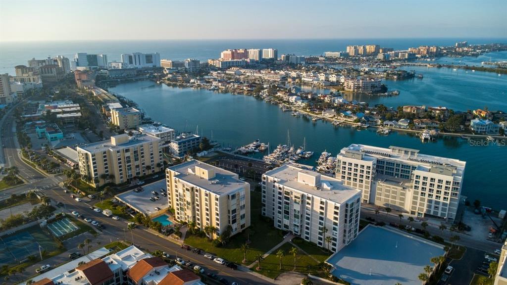 An aerial view of a coastal city featuring multi-story apartment buildings, a marina, and water — 830 S GULFVIEW BOULEVARD UNIT 502, CLEARWATER BEACH, FL