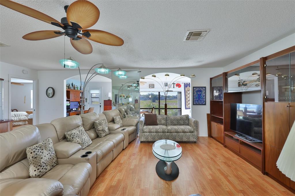 A living room features a beige leather sectional, patterned sofa, wood flooring, and wall mirrors — 2611 LANCASTER DRIVE UNIT 33, SUN CITY CENTER, FL