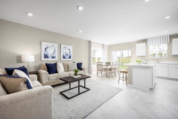 An open-concept living room features a beige sofa, coffee table, and adjacent kitchen with white cabinets — PORT ST. LUCIE, FL