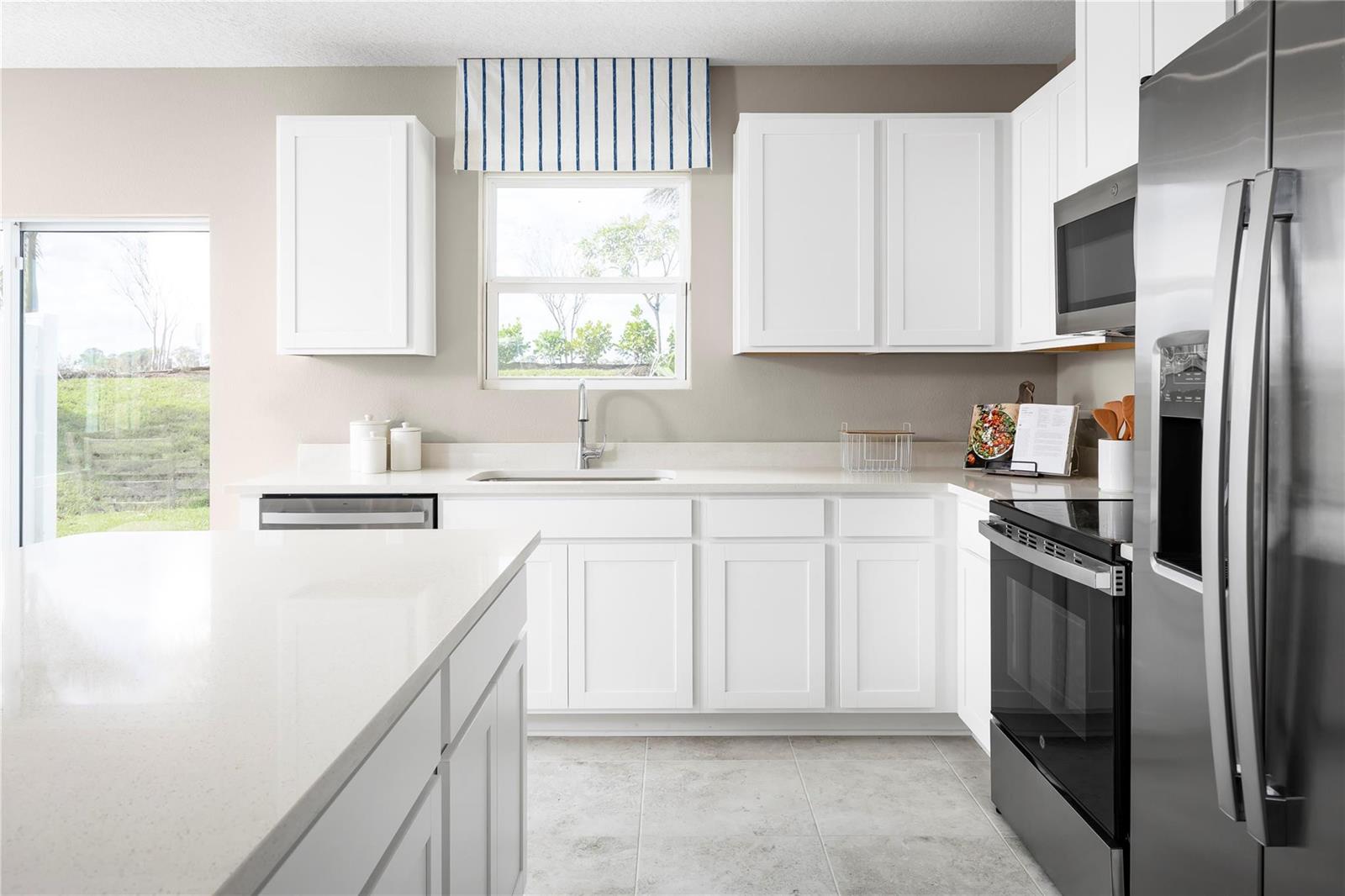 A kitchen features white cabinets, stainless steel appliances, quartz countertops, and a window with valance — PORT ST. LUCIE, FL