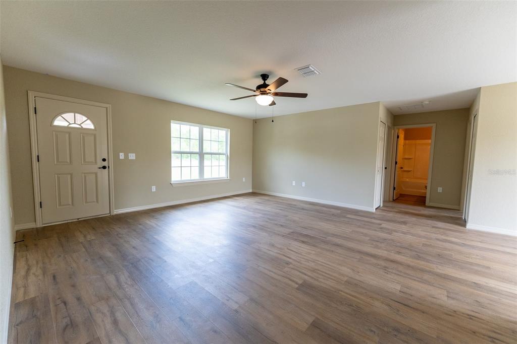 An empty room with light wood-look flooring, beige walls, a ceiling fan, and a door — 14686 SW 79TH AVENUE ROAD, OCALA, FL