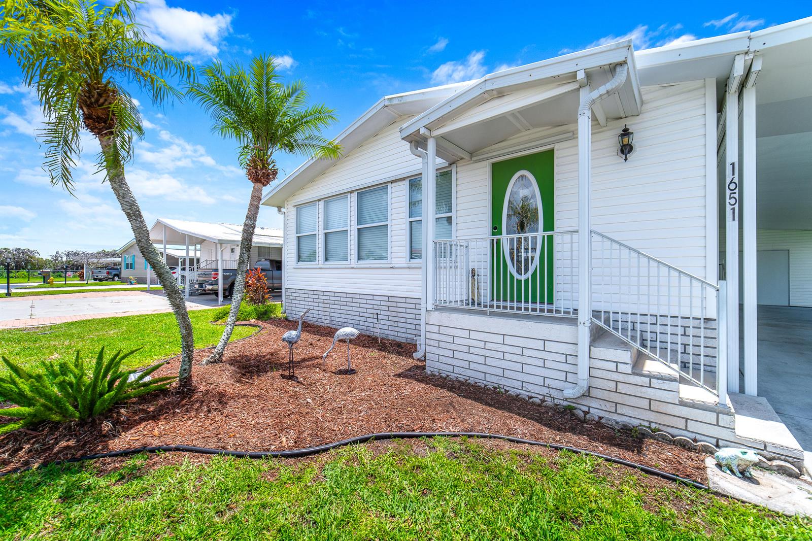 A white mobile home exterior features a green front door, palm trees, and lawn ornaments — 1651 SW 35th Circle, Okeechobee FL 34974, OKEECHOBEE, FL