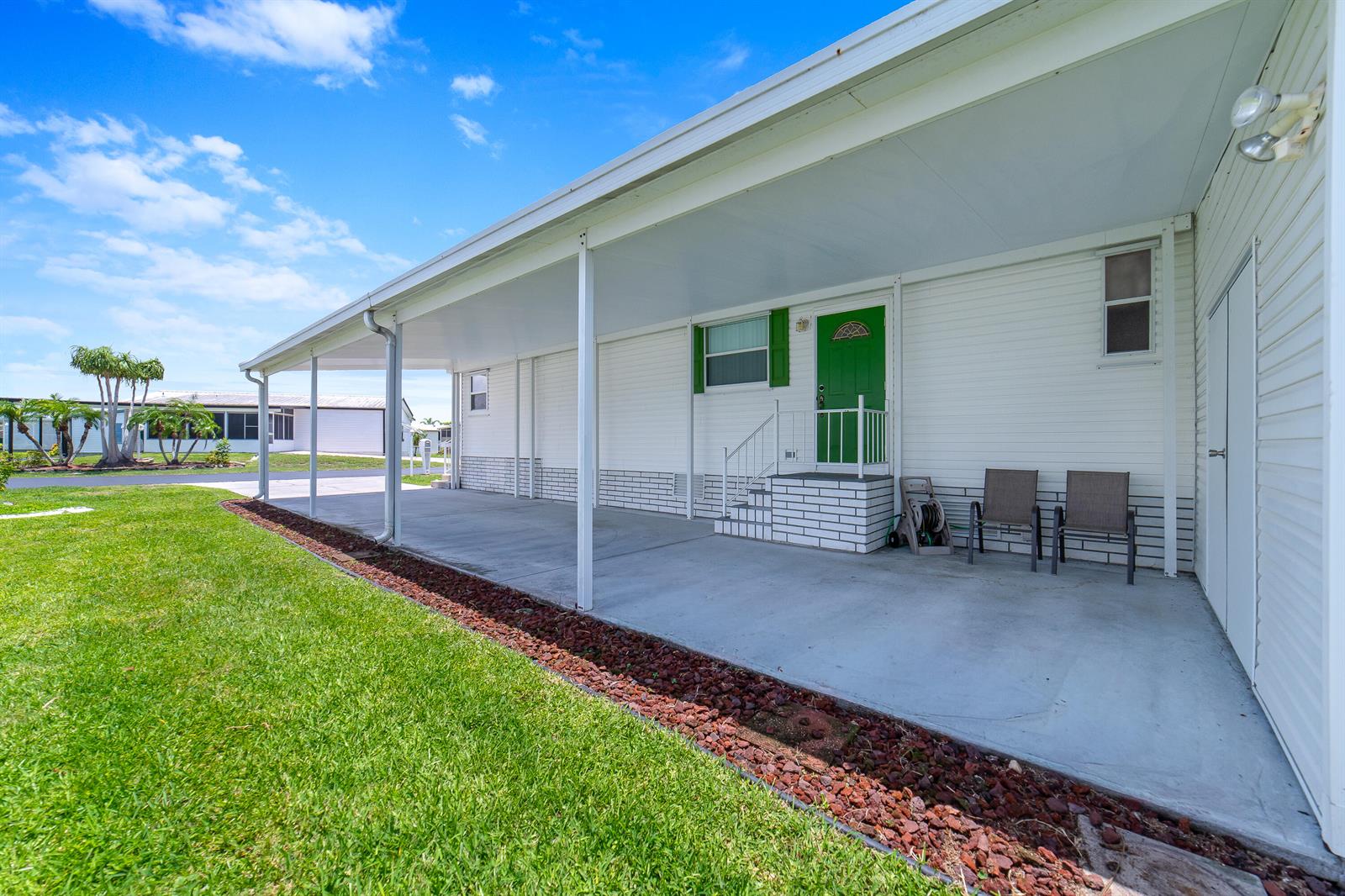 A white mobile home features a concrete carport, a green front door, and two chairs — 1651 SW 35th Circle, Okeechobee FL 34974, OKEECHOBEE, FL